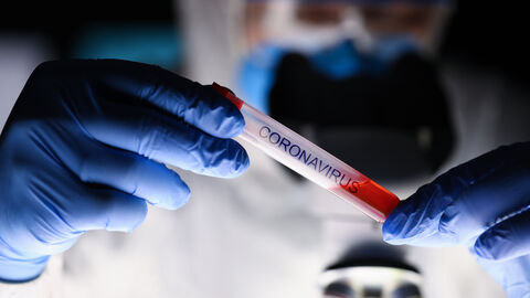 Hände in blauen Handschuhen halten eine Ampulle mit der Aufschrift "Coronavirus"