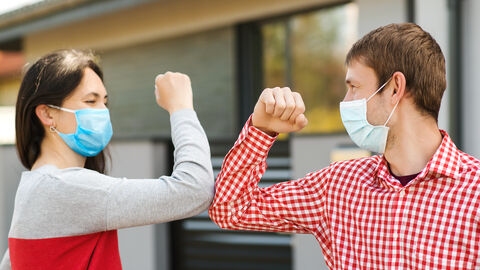 Eine Frau und ein Mann mit Maske grüßen sich per Ellenbogen