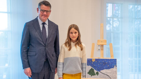 Boris Rhein und die neunjährige Amelie stehen neben dem gemalten Winter-Bild, beide gucken in die Kamera