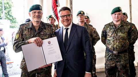 Veteranentag Hessentag 2025 Ministerpräsident Boris Rhein hält mit einem Mann von der Bundeswehr eine Urkunde in die Kamera.