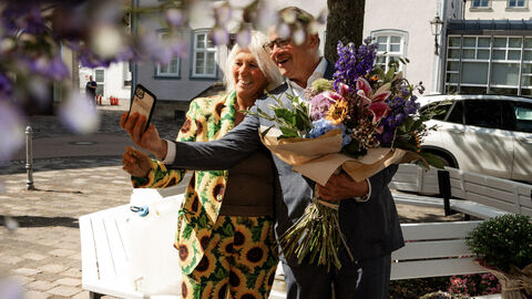 Ein Mann steht neben einer Frau mit einem Blumenstrauß und macht ein Selfie,