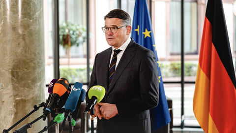 Ministerpräsident Rhein steht vor Mikrofonen in einer Interviewsituation.