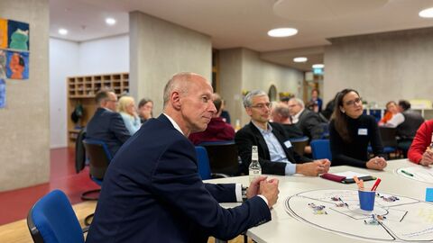 Bildungsminister Schwarz sitzt mit weiteren Personen an einem Tisch zur Diskussion.