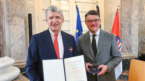 Zwei Männer stehen nebeneinander und halten eine Urkunde hoch.