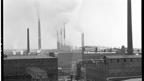 Schwarz-Weiß-Aufnahme mit Ausblick auf ein Industriegebiet in den 60er Jahren. Schmale Schornsteine ragen in den Himmel.