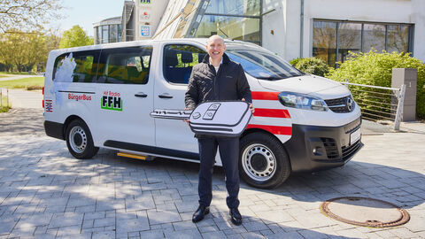 Ministr Pentz steht vor einem Kleinbus mit einem überdimensionierten Autoschlüssel in Händen.