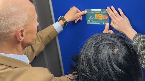 Bildungsminister Armin Schwarz und Jonathan Schnaus bringen einen Sticker mit der „Nummer gegen Kummer“ an. 